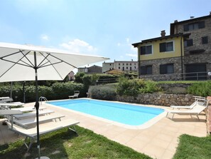 A swimming pool with lounge chairs and an umbrella, surrounded by a stone wall and greenery.
