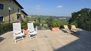 Une terrasse avec des chaises blanches et une vue sur un paysage vallonné.
