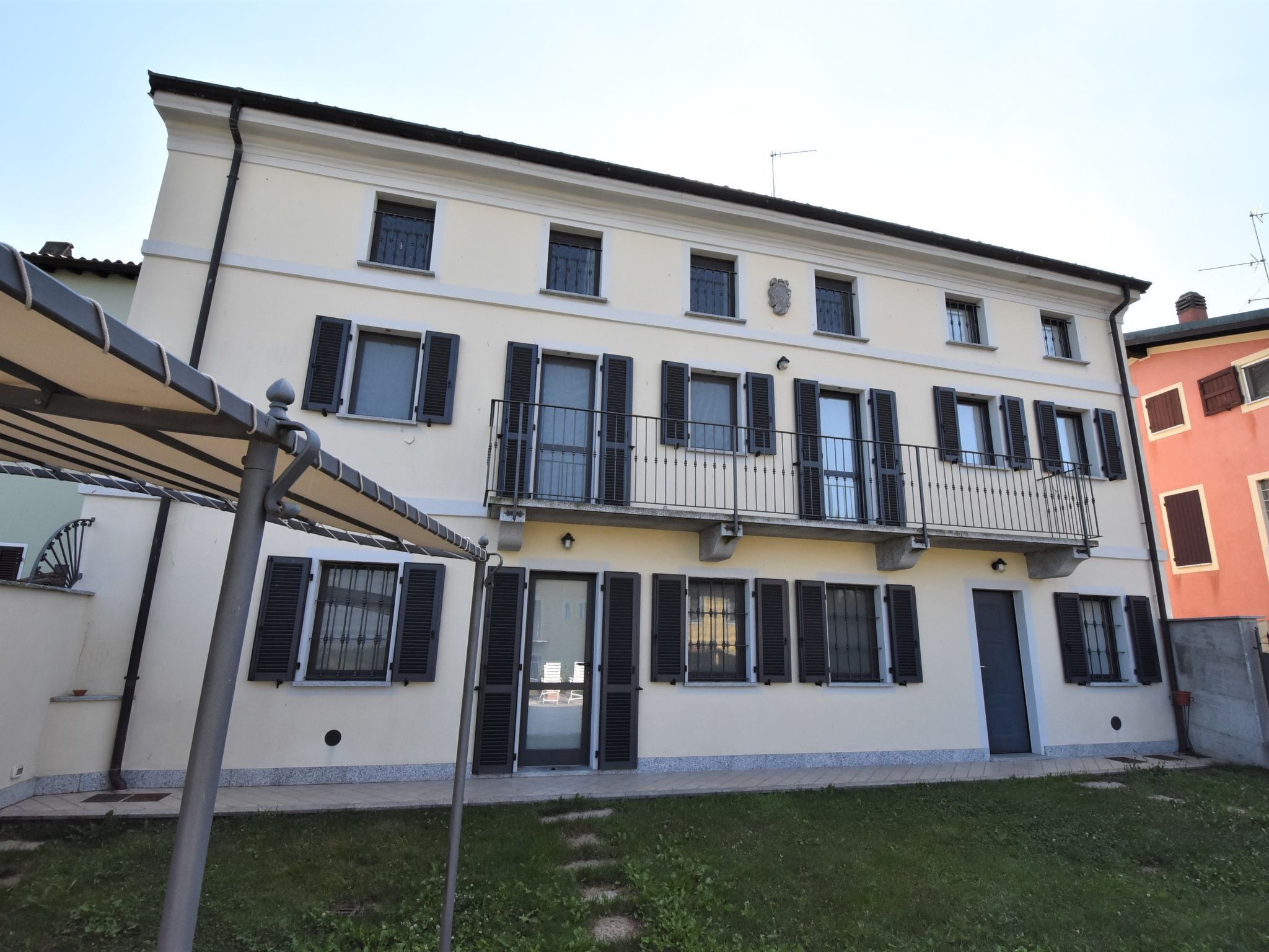 A multi-story building with balconies, a flat roof, and a small garden area in front.