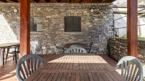 A covered patio with a stone wall, wooden table, and chairs.