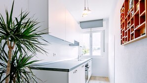 Una cocina estrecha con armarios blancos, una ventana y una planta.