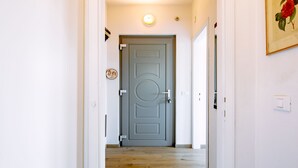 A hallway with a wooden floor, a grey door, and a light fixture on the wall. - Villetta ai Pini by Interhome (Lago di Caldonazzo)