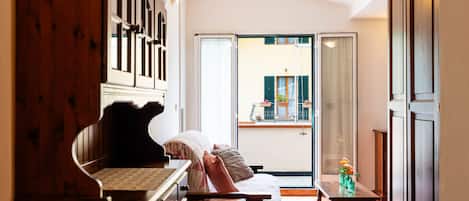 A cozy living room with a piano, a sofa, and a dining table. There is a large window with a view of the outside.