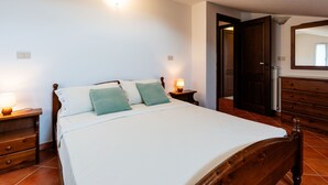 Um quarto com uma cama de madeira, duas mesas de cabeceira com luminárias, um aparador e um espelho na parede.