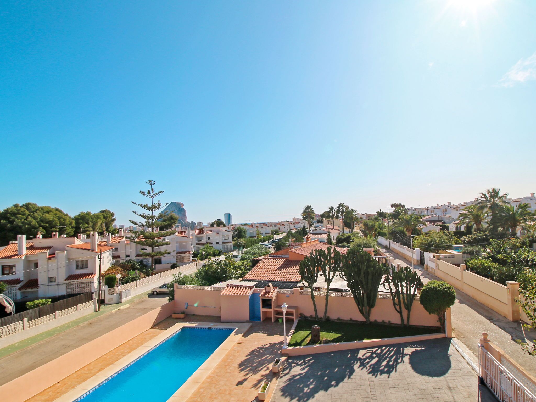A residential area with a swimming pool, houses with red-tiled roofs, and palm trees.