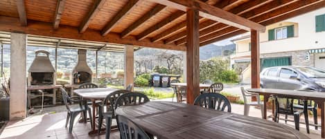 An outdoor patio with wooden tables and chairs, a stone oven, and a view of a residential area.