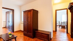 Quarto espaçoso com um grande guarda-roupa de madeira, uma mesinha com um vaso de flores e uma área de refeições visível por uma porta aberta.
