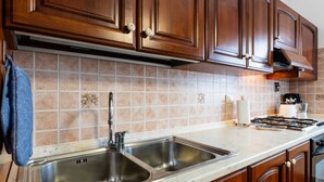 Eine Küche mit Holzausbau, einem Edelstahlspülbecken, einem Gasherd und einer gefliesten Spritzschutzwand.