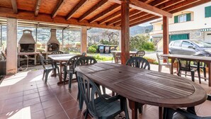 Eine Terrasse im Freien mit Holztischen und -stühlen, einem Steinkamin und Blick auf einen Berg sowie ein geparktes Auto.