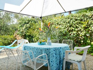 An outdoor patio with a round table covered by a blue floral tablecloth, surrounded by white metal chairs.