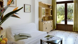 A room with a white sofa, a wooden cabinet with a mirror, a small table with bowls, and a large window with curtains. - Ivano (PGI125) by Interhome (Poggi)