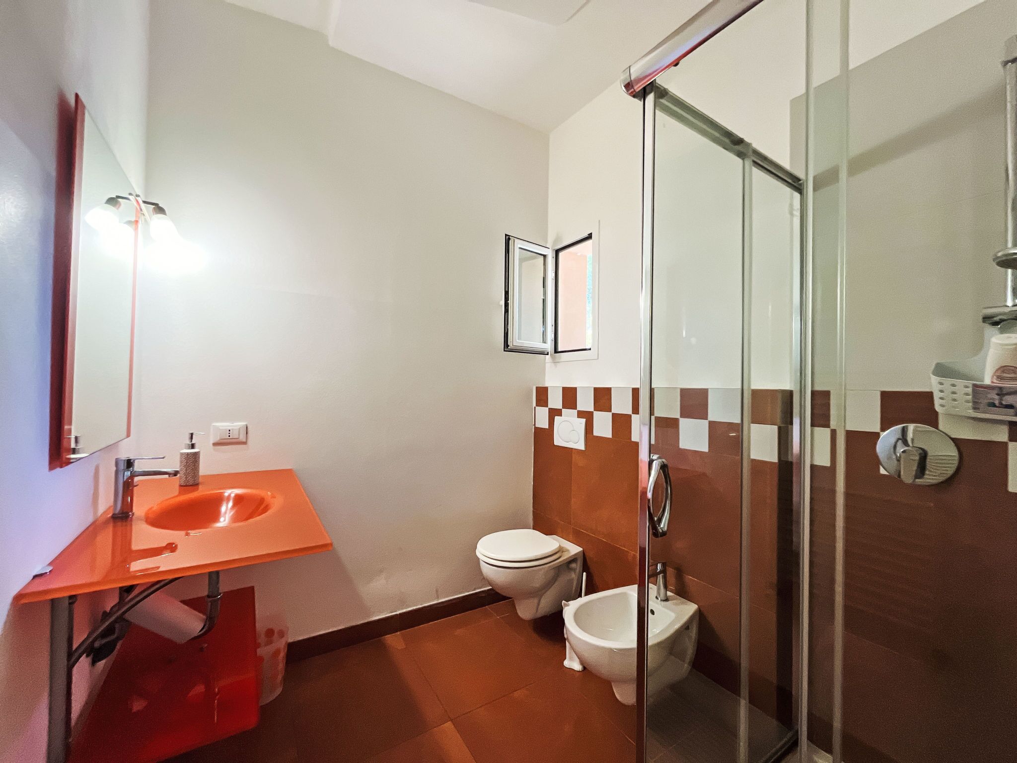 Un bagno con box doccia in vetro, un water bianco e un lavandino arancione.