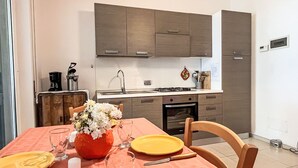 Une cuisine moderne avec des meubles gris, un plan de travail blanc et une table à manger agrémentée d’assiettes jaunes et d’un vase de fleurs.