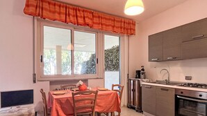 Une cuisine compacte avec un coin repas, une fenêtre avec des rideaux, un téléviseur et une cuisinière.