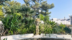 A garden with a stone wall, various plants, and a statue. - Blu Mediterraneo (PGI210) by Interhome (Poggi)
