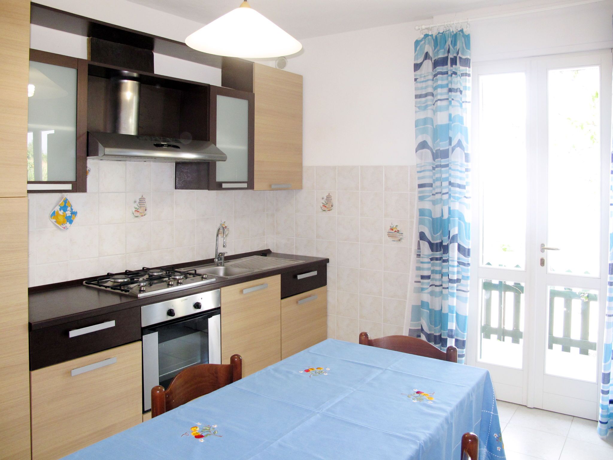 A kitchen with a gas stove, oven, and modern cabinetry. There is a dining table with a blue tablecloth and chairs.