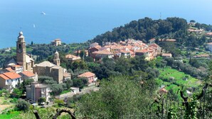 A coastal village with traditional architecture, a prominent church tower, and a view of the sea. - Primavera (PGI132) by Interhome (Poggi)