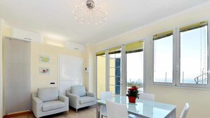 A modern living room with a glass dining table, two sofas, and a view of the sea through large windows. - Primavera (PGI132) by Interhome (Poggi)