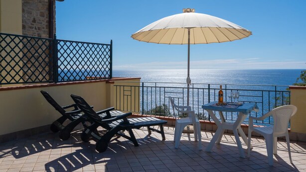 A balcony with a table, chairs, and an umbrella overlooking the sea. - Primavera (PGI132) by Interhome (Poggi)