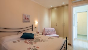 A bedroom with a bed, a nightstand, a wall-mounted lamp, a wardrobe, and a door leading to another room. - Primavera (PGI132) by Interhome (Poggi)