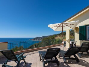 A balcony with lounge chairs, a table, and an umbrella overlooking a coastal view. - Primavera (PGI130) by Interhome (Poggi)