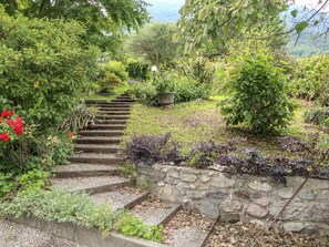 Una escalera de piedra que asciende por una colina, rodeada de vegetación exuberante y plantas en flor.
