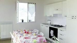 A kitchen with white cabinets, a gas stove, and a window with curtains. - Luca (PRE171) by Interhome (Molini di Prelà)