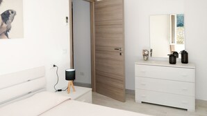 Quarto moderno com porta de madeira, cômoda branca, mesa de cabeceira e ar condicionado fixado na parede.