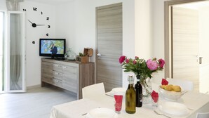 Uma sala de jantar com uma mesa posta para dois, uma televisão na parede e um armário de madeira com objetos decorativos.
