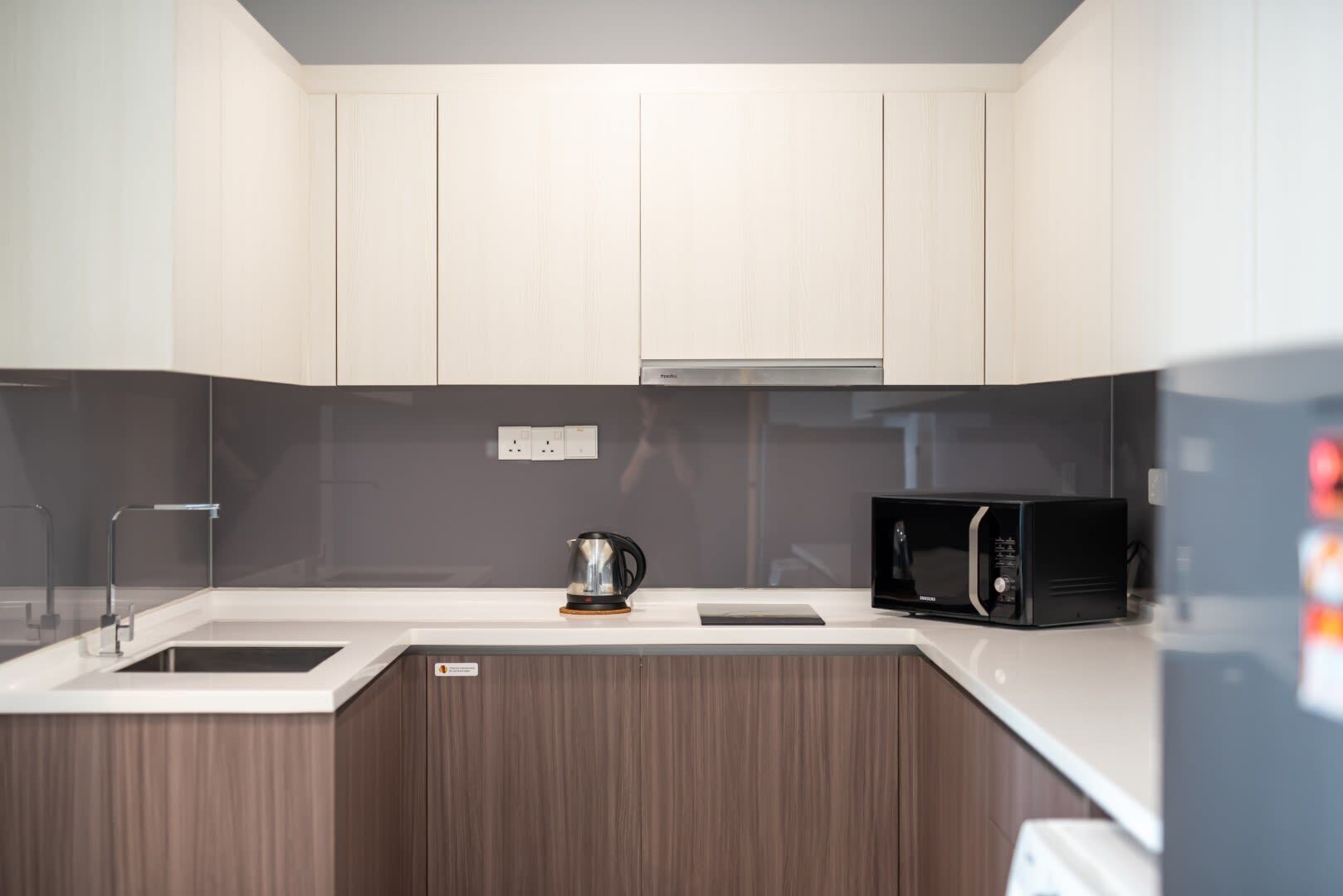 A modern kitchen with white cabinets, a stainless steel kettle, a black microwave, and a built-in oven.