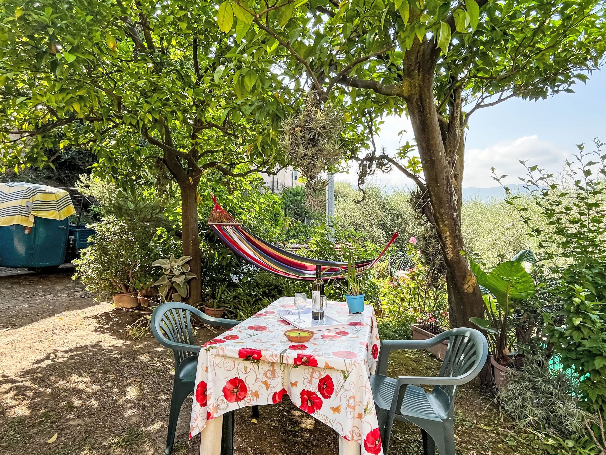 Ein Garten mit Tisch für Mahlzeiten, umgeben von viel Grün und einer Hängematte.