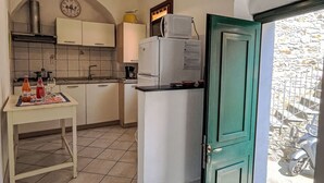 A compact kitchen with a refrigerator, a coffee maker, and a small table with bottles and glasses. - Elisa (DOL127) by Interhome (Dolcedo)