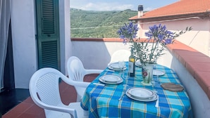 Un balcon avec une table dressée pour le repas, des chaises et un pot de fleurs.