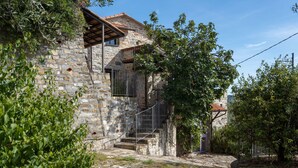 A stone building with a rustic exterior, a wooden staircase leading to a balcony, and a garden area with trees and shrubs. - U Figu du Camin by Interhome (Pontedassio)