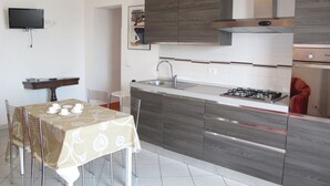 A modern kitchen with a dining area, featuring a flat-screen TV, a gas stove, and a sink. - Orange (SLR353) by Interhome (San Lorenzo al Mare)