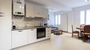 Une cuisine moderne avec des meubles blancs, une cuisinière à gaz et un four à micro-ondes. On y trouve également un coin repas avec une table et des chaises.