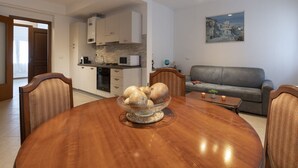 Un salon moderne avec une table à manger en bois, un canapé gris et une cuisine en arrière-plan.