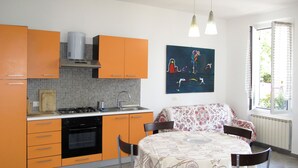 A kitchen with orange cabinets, a stove, and a sink. There is a dining table with chairs and a painting on the wall.