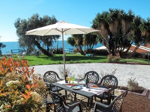 Un patio al aire libre con mesa y sillas, una sombrilla blanca y vistas al mar.