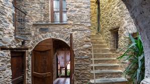 Um edifício de pedra com um arco de entrada, uma porta de madeira e uma escadaria que leva a um andar superior.