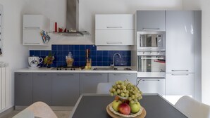 Een moderne keuken met grijze kastjes, een blauwe betegelde spatwand en roestvrijstalen apparatuur.
