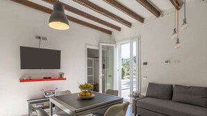 Een moderne woonkamer met een eethoek, houten balken, een flatscreen-tv, een rode plank en een glazen deur naar buiten.