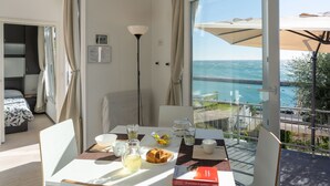 Een balkon met een ontbijttafel, een bed en uitzicht op zee.
