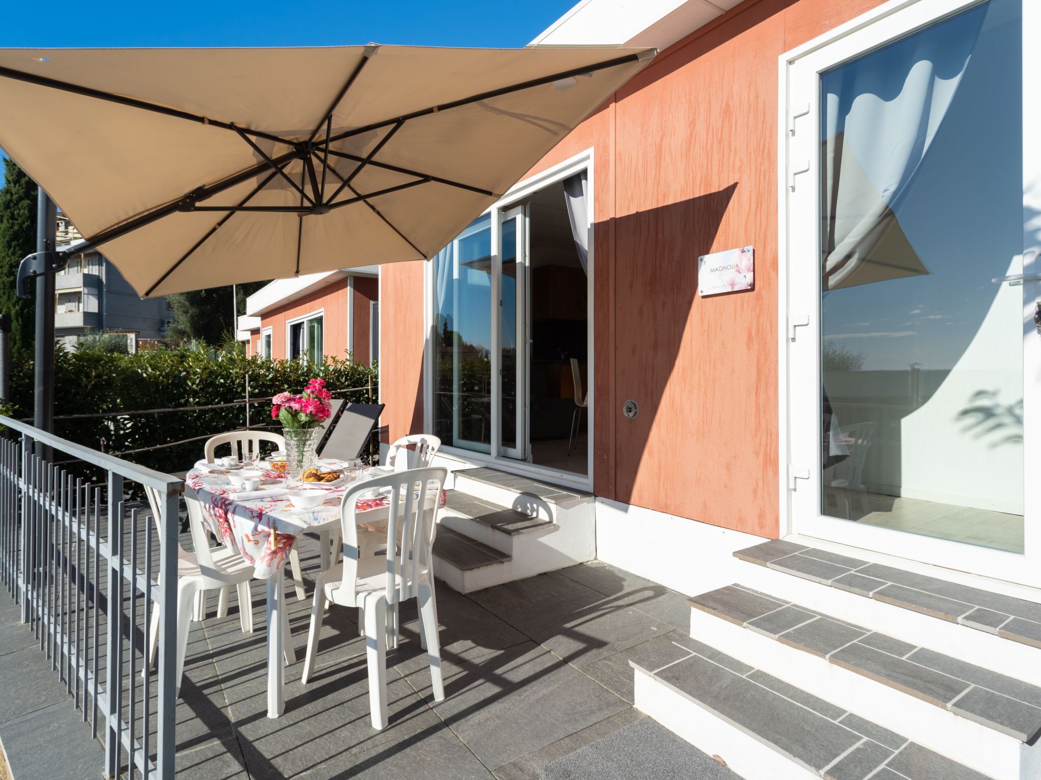 A balcony with a table and chairs, a large umbrella, and a building with a sign reading "MAGNOUA".