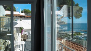Ein Balkon mit Blick auf das Meer und Boote, weiße Stühle und ein Tisch.