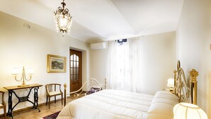 A spacious bedroom with a large bed, a chandelier, a wooden chair, a small table with a lamp, and a painting on the wall. - San Giacomo by Interhome (San Damiano d'Asti)