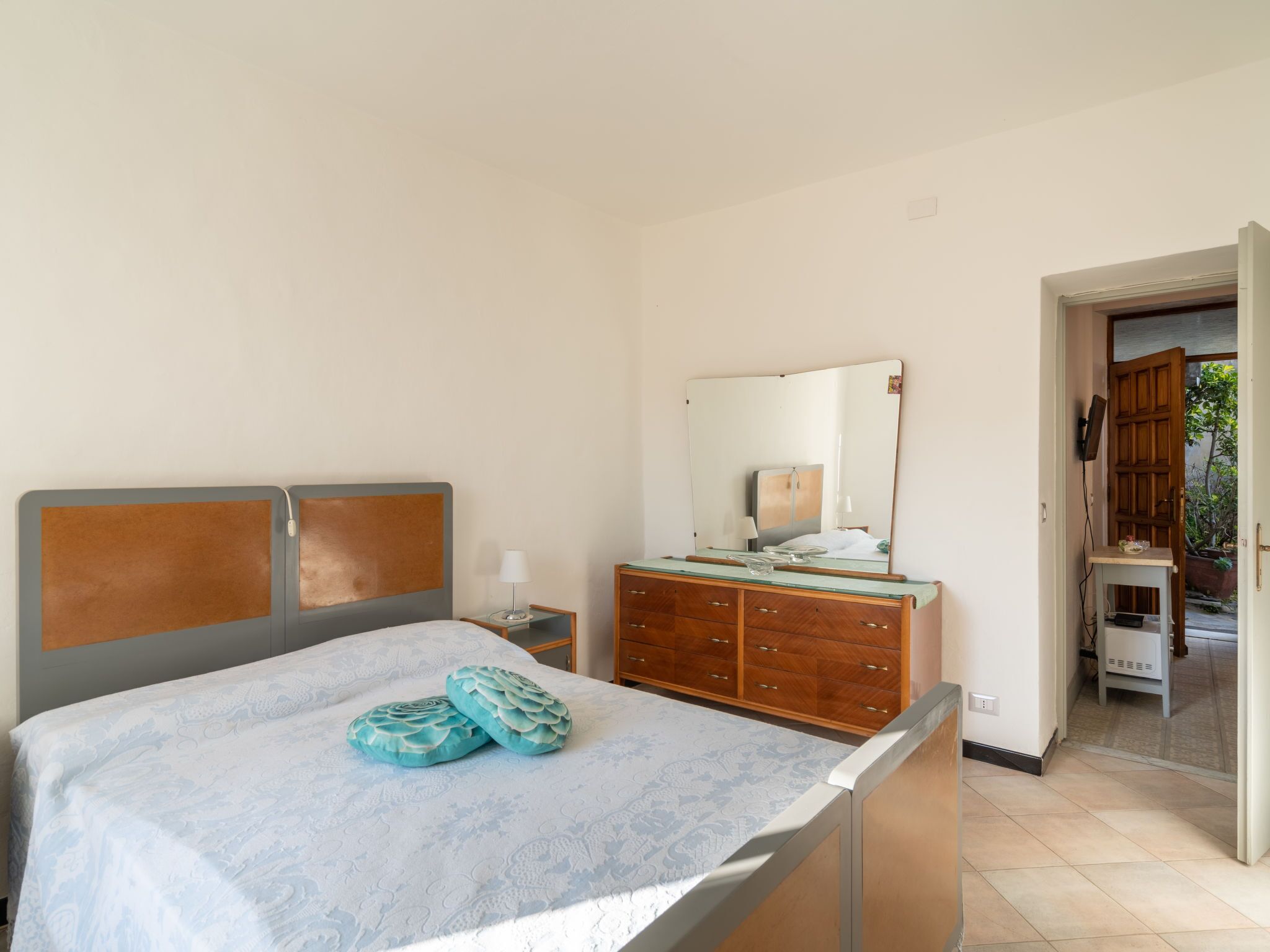 A bedroom with a bed, a dresser, a mirror, and a door leading to a balcony.