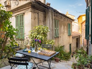A courtyard with a table set for breakfast, surrounded by greenery and historic buildings. - Caruggiu (PTB193) by Interhome (Pietrabruna)