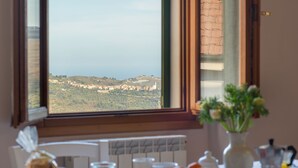 Une table à manger dressée avec des aliments pour le petit-déjeuner, et une vue sur un paysage côtier par la fenêtre.
