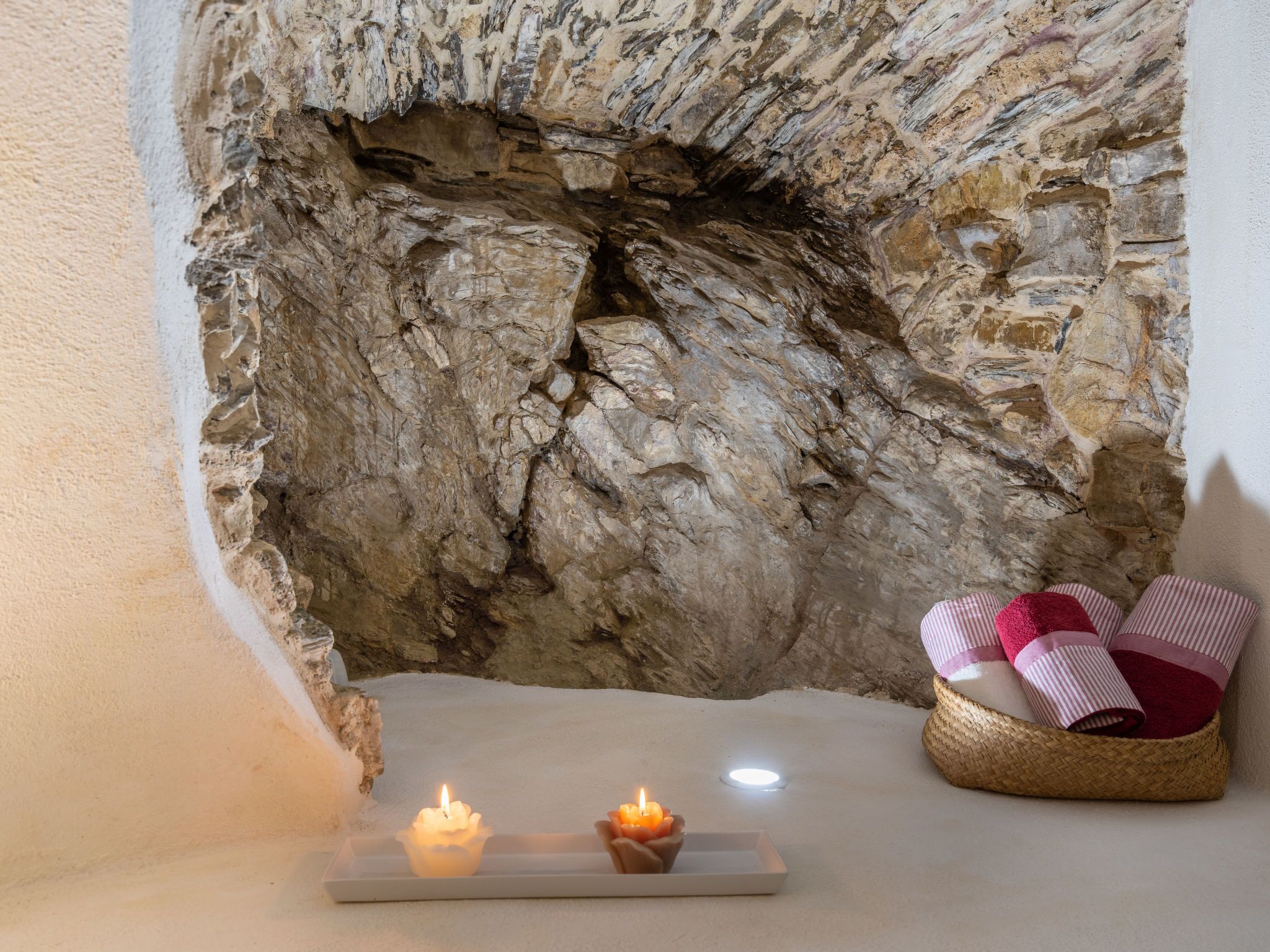 Una habitación acogedora con pared de piedra, una mesa iluminada por velas y una cesta de toallas.